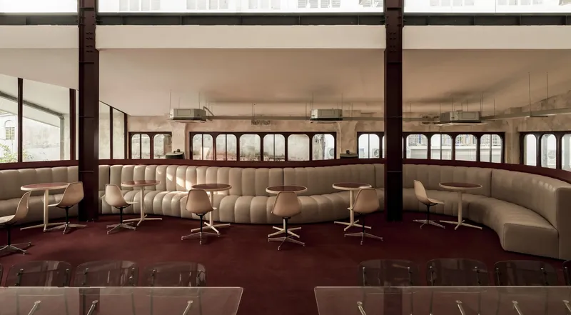 Continuous curved banquette seating with pedestal tables along perimeter windows framed by exposed structural columns