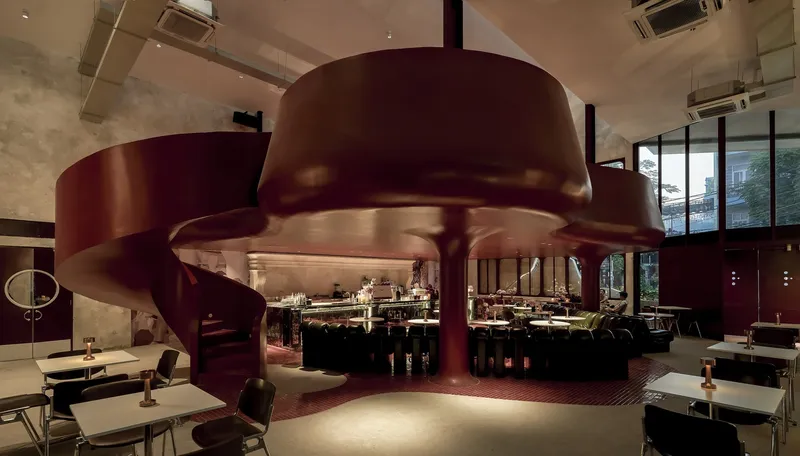 Sculptural helical staircase in burgundy metal descending from an upper mezzanine level into the dining room