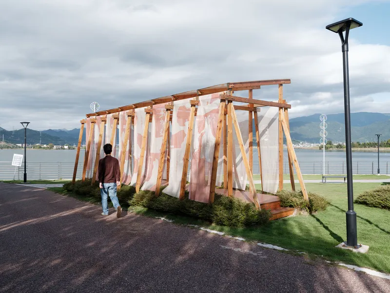 Visitor approaching the timber pergola structure with draped fabric under an overcast sky