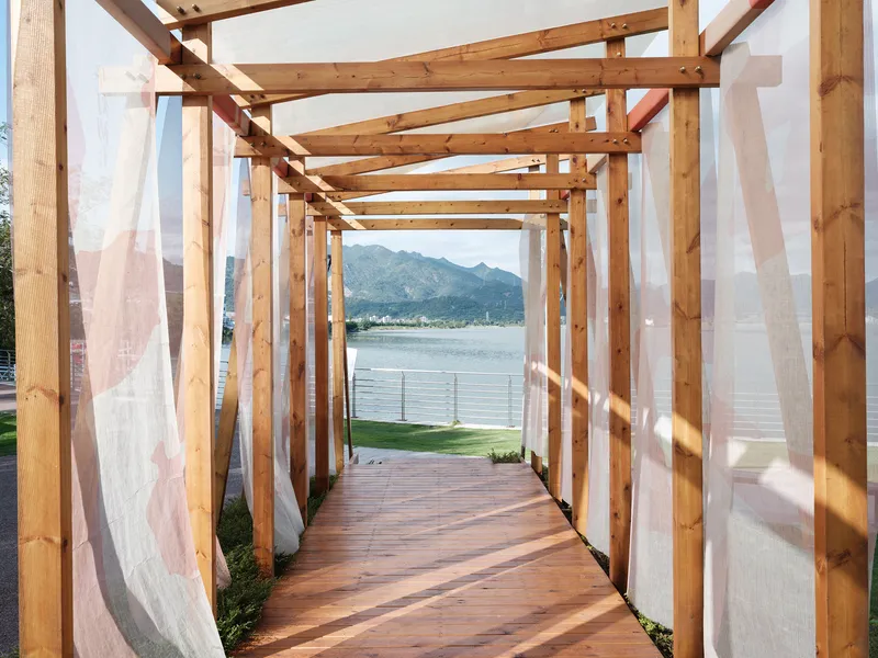 Interior walkway through the timber frame pavilion with fabric curtains filtering sunlight toward the lake