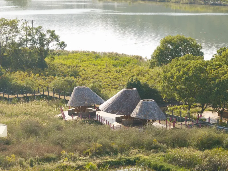 Aerial view of three thatched roof pavilions nestled among trees beside a calm lake