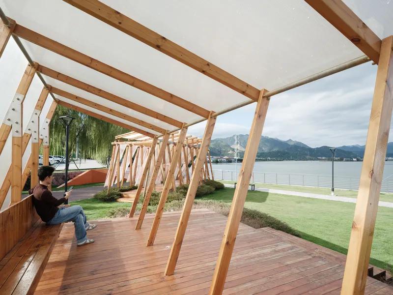 Covered timber deck with diagonal bracing and fabric canopy where a visitor sits overlooking the water
