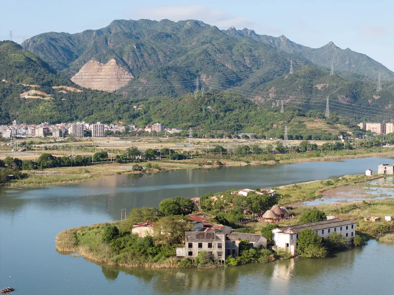Riverside cluster of thatched and tiled roof buildings on a small island with mountains beyond