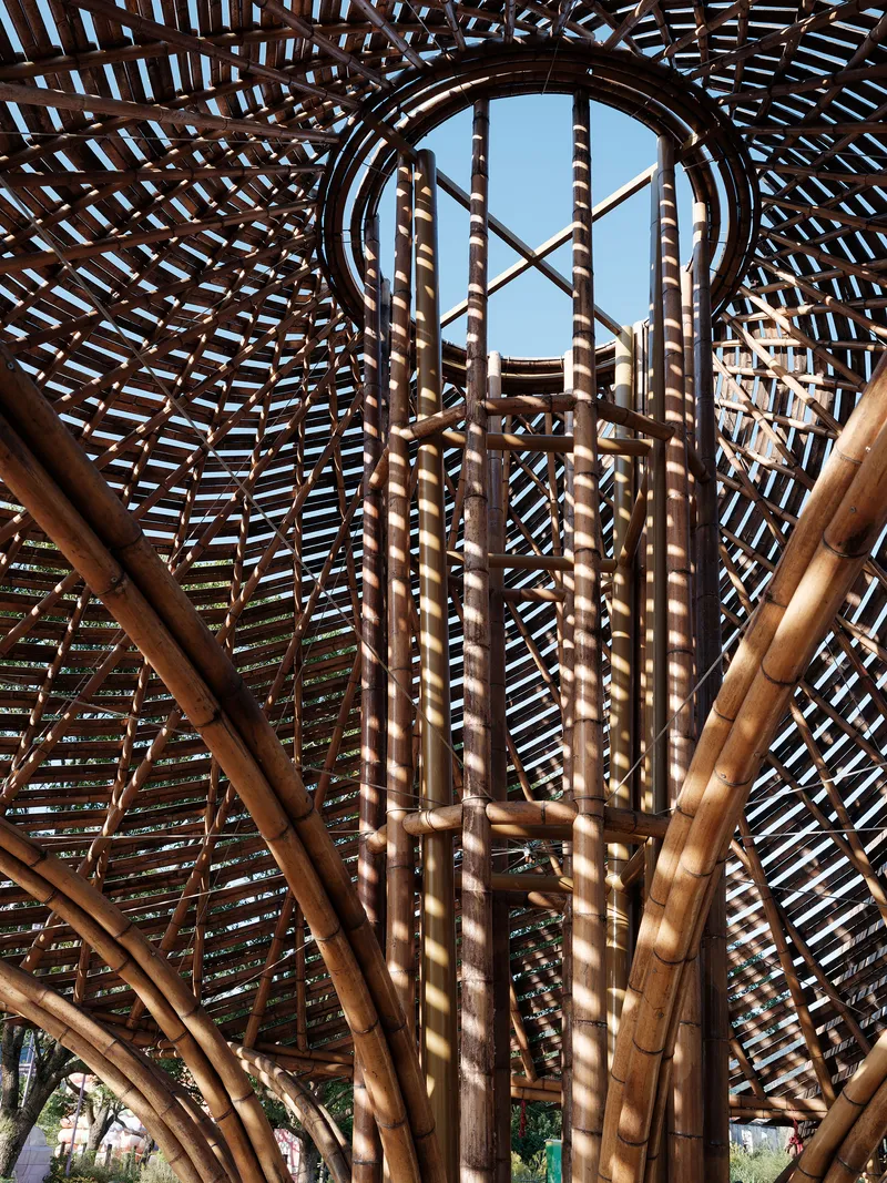 Interior view looking up through bundled bamboo columns and latticed roof structure to a circular oculus