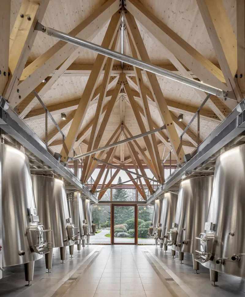 Central aisle flanked by stainless steel fermentation vessels beneath exposed timber roof trusses