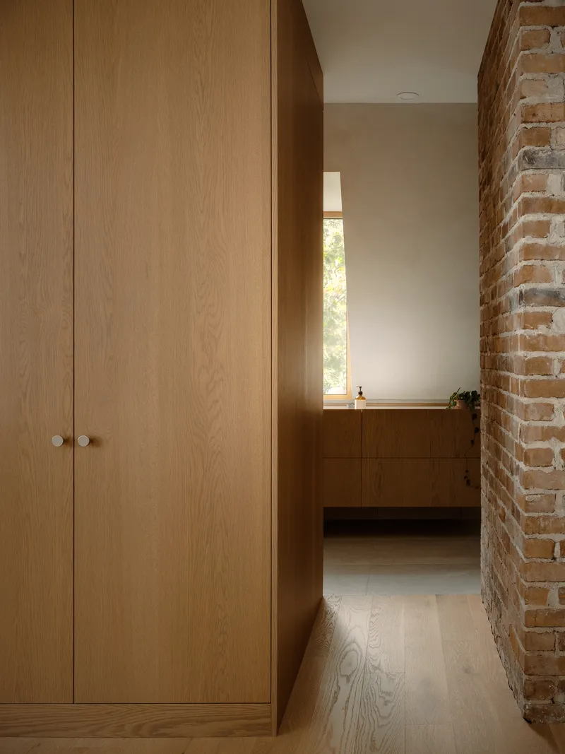 Oak cabinetry lining a narrow hallway beside an exposed brick wall in afternoon light