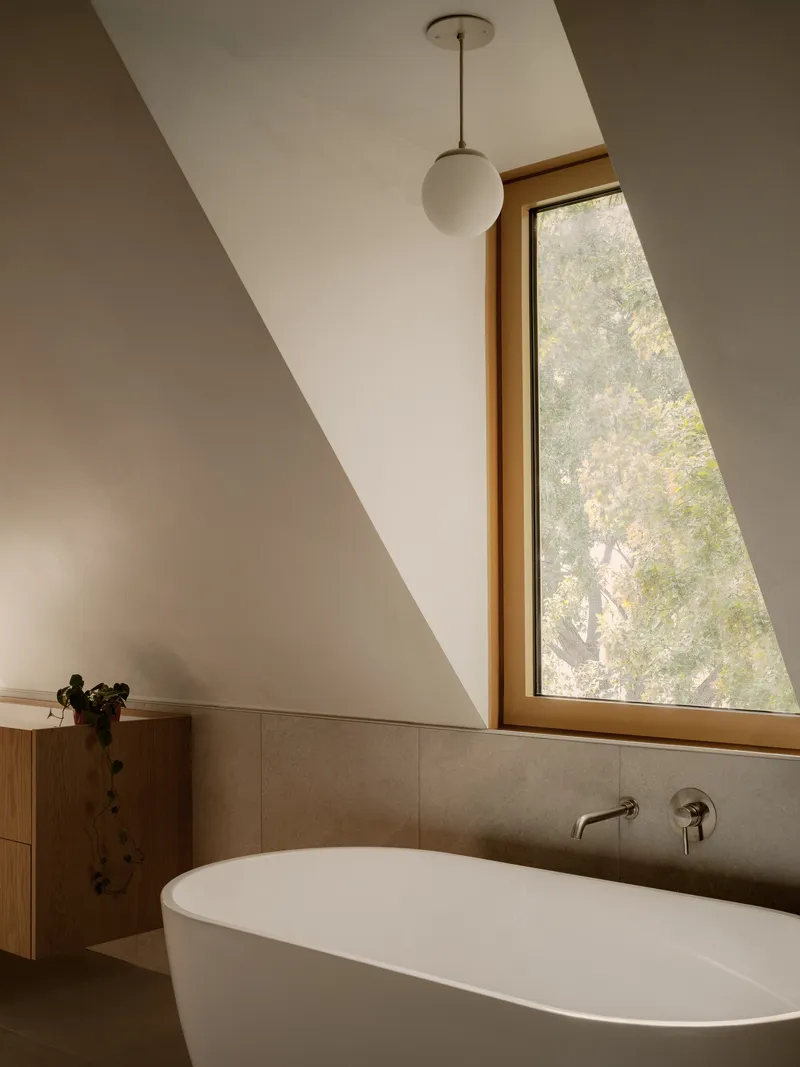 Triangular window framing autumn foliage above a tub with wall-mounted faucet