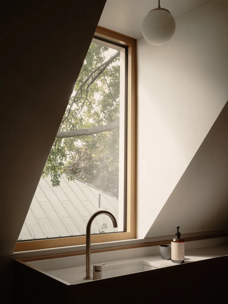 Angled window with timber frame above a recessed sink looking out to tree branches