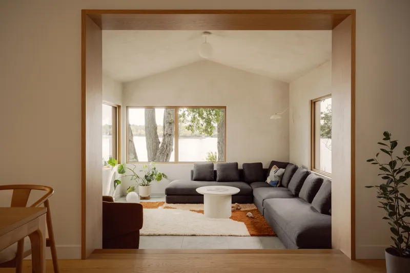 Living room framed by timber portal with vaulted white ceiling and sectional sofa facing lakeside windows