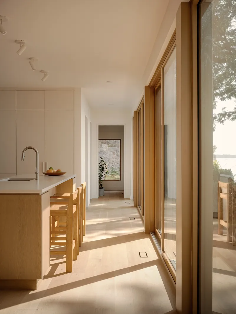 Kitchen corridor with timber-framed glazing casting morning shadows across pale flooring and white cabinetry