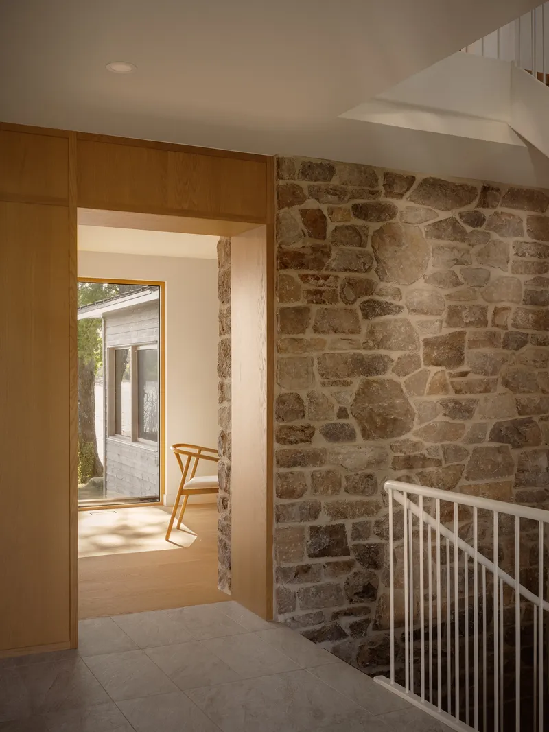 Stairwell landing with exposed stone wall and timber-framed doorway opening to exterior deck beyond