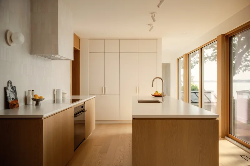 Kitchen with oak cabinetry and white countertops opening to glazed doors facing the waterfront