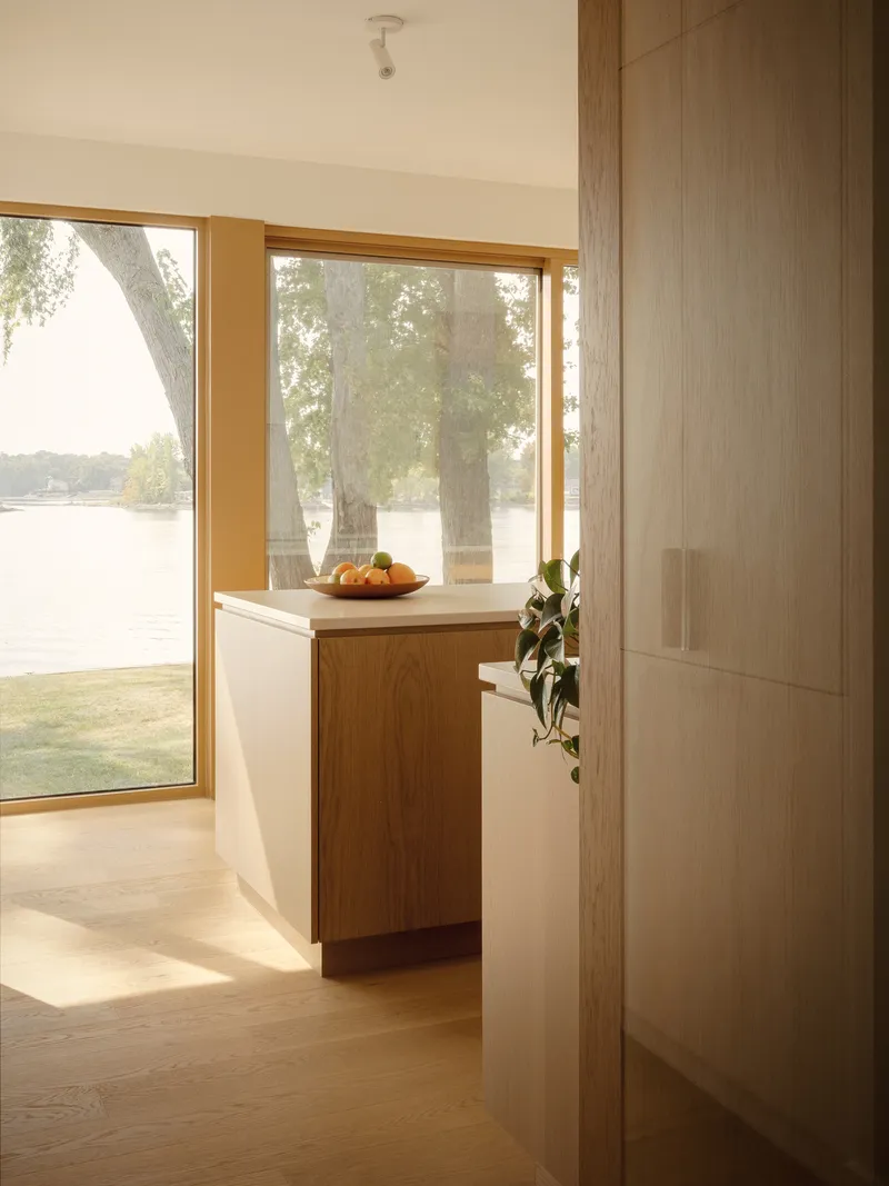 Hallway corner with oak storage cabinet and timber-framed window overlooking a lakeside lawn