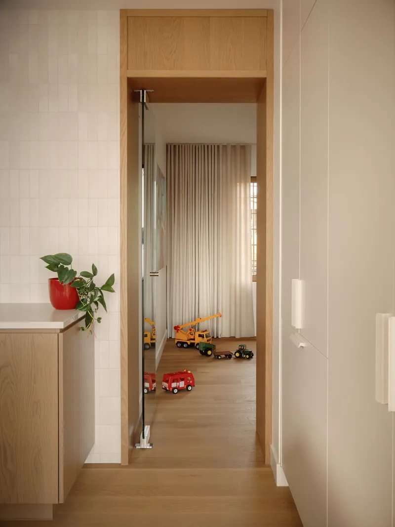View through oak-lined doorway into bedroom with fluted curtain and toy vehicles on floor