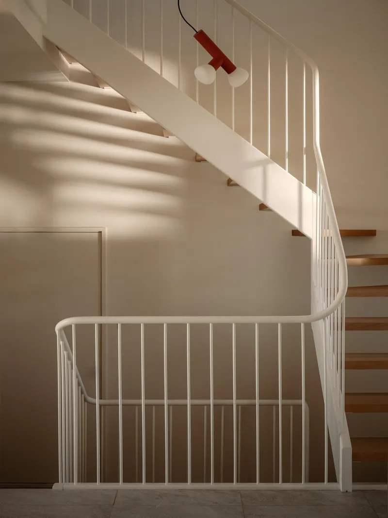 Curved staircase with white metal balustrade and timber treads beneath a red pendant light