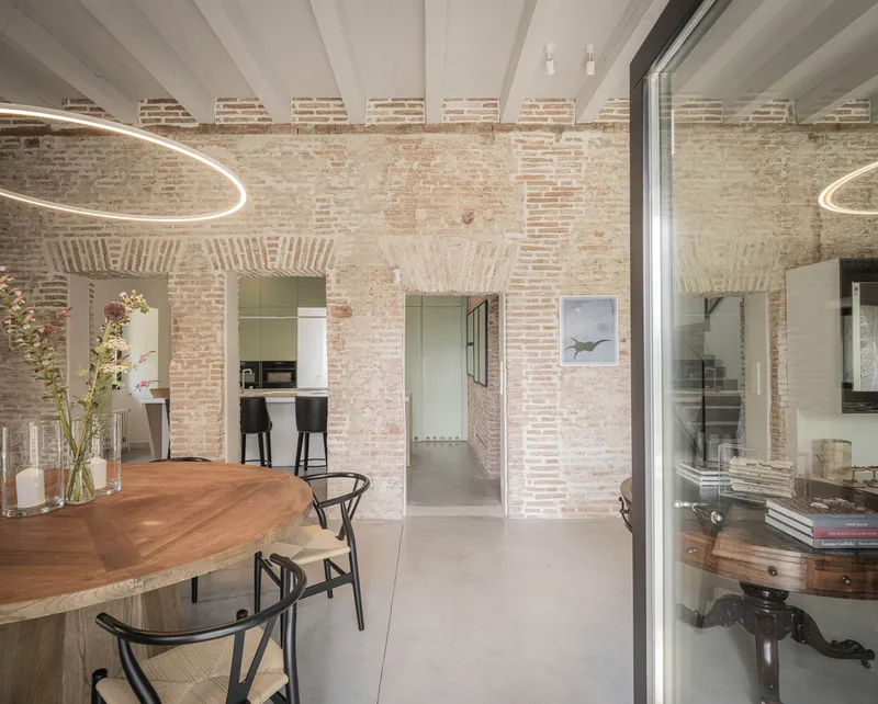 Dining area with exposed brick walls and timber ceiling beams beneath circular pendant lighting