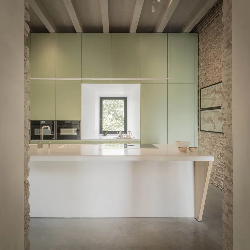 Kitchen island with pale green cabinetry framed by exposed brick columns and timber ceiling