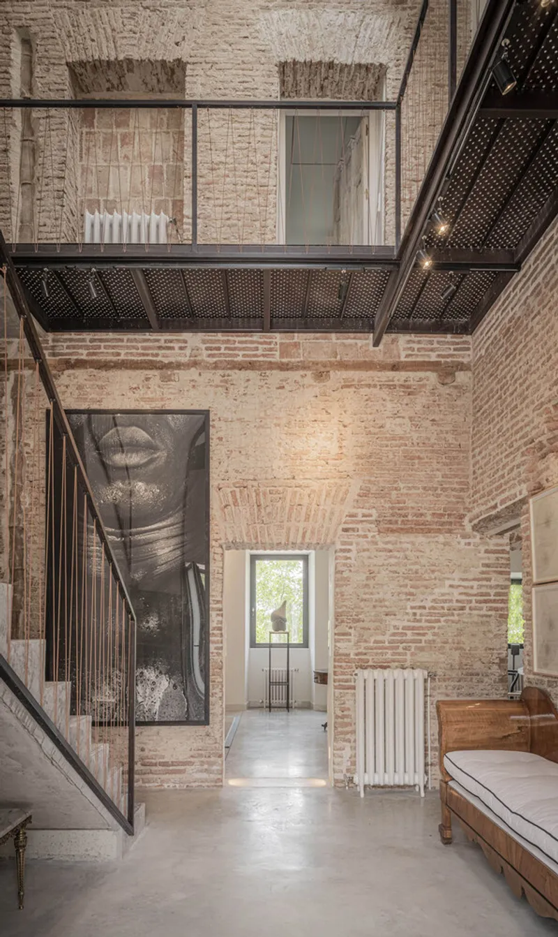 Double-height interior void with exposed brick walls and perforated metal balcony overlooking entrance hallway