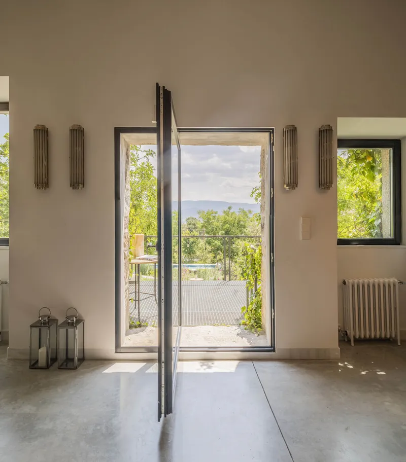 Open glass door leading to outdoor deck with trees and distant hills visible in afternoon sunlight