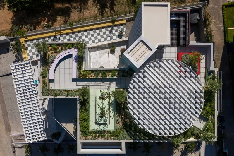 Aerial view showing the circular checkered roof alongside rectangular volumes and courtyard gardens with planted trees