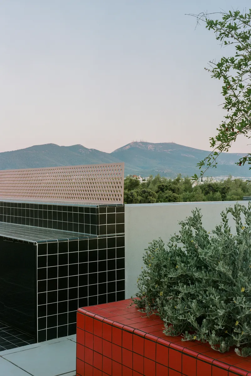 Rooftop terrace with dark green tile wall, red tile planter and perforated screen under a mountain skyline