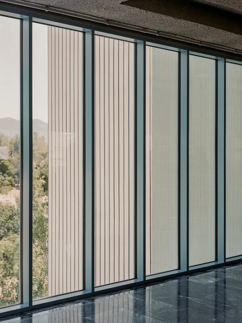 Floor-to-ceiling windows with vertical fluted glass panels and dark metal frames reflecting green landscape