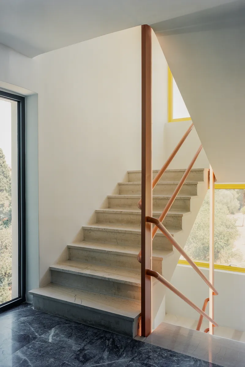 Internal staircase with light stone treads and terracotta metal railing with geometric yellow accent bands