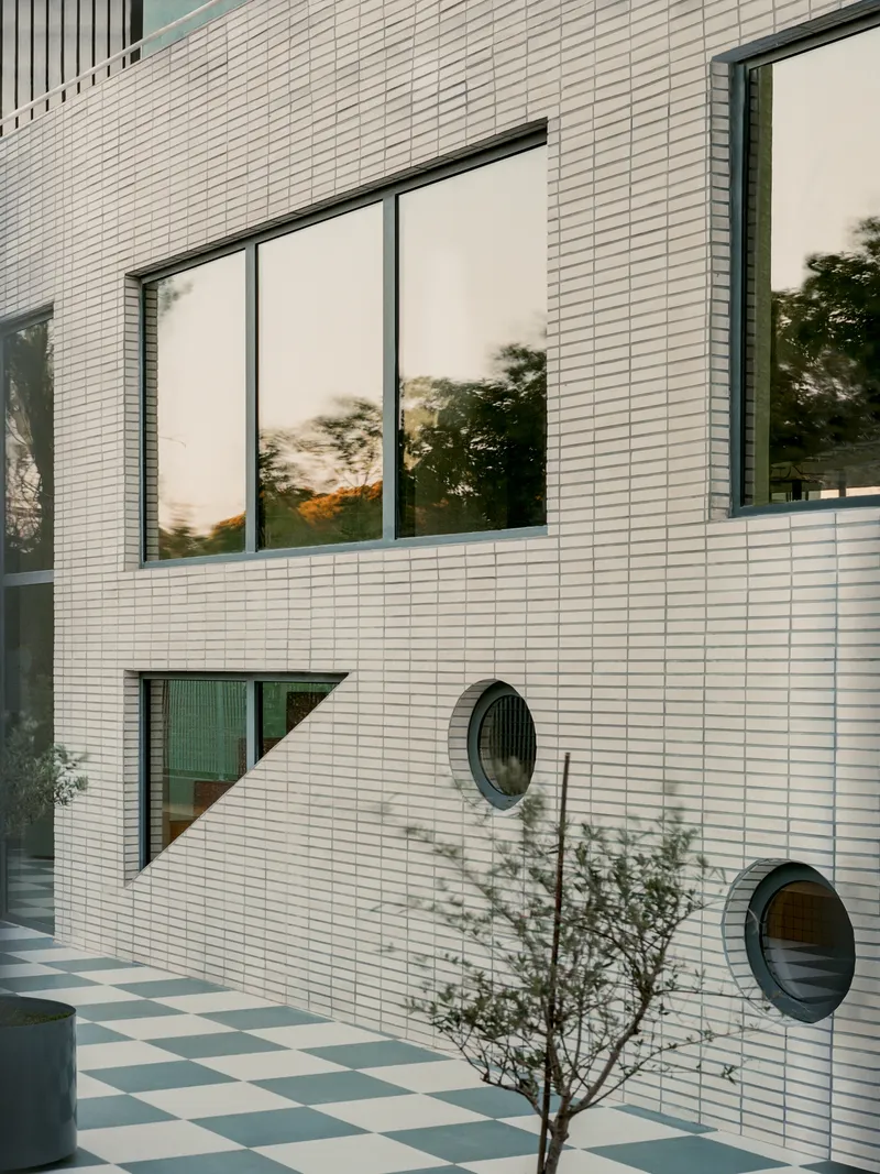 White brick facade with rectangular window, two circular openings and tree reflections at dusk