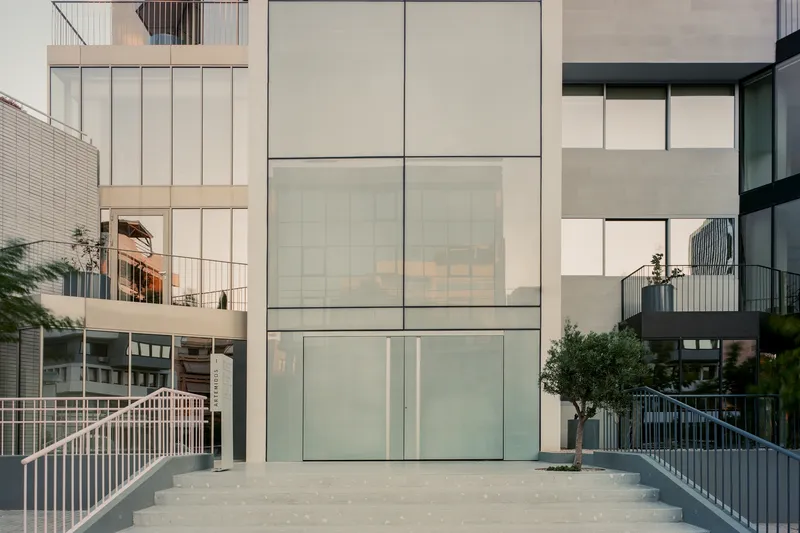Courtyard view showing stacked balconies with metal railings and translucent glass volumes flanking a planted tree