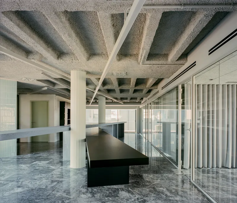 Interior workspace with exposed coffered concrete ceiling, white columns, black tables and marble flooring