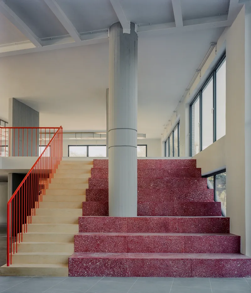 Lobby staircase with red terrazzo treads, light wood risers, red metal railing and central cylindrical column
