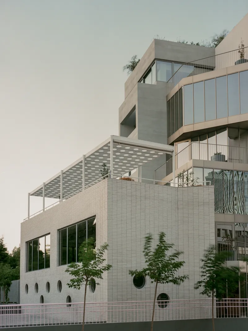 Stacked balconies with white tile cladding and circular openings beneath a perforated canopy at dusk