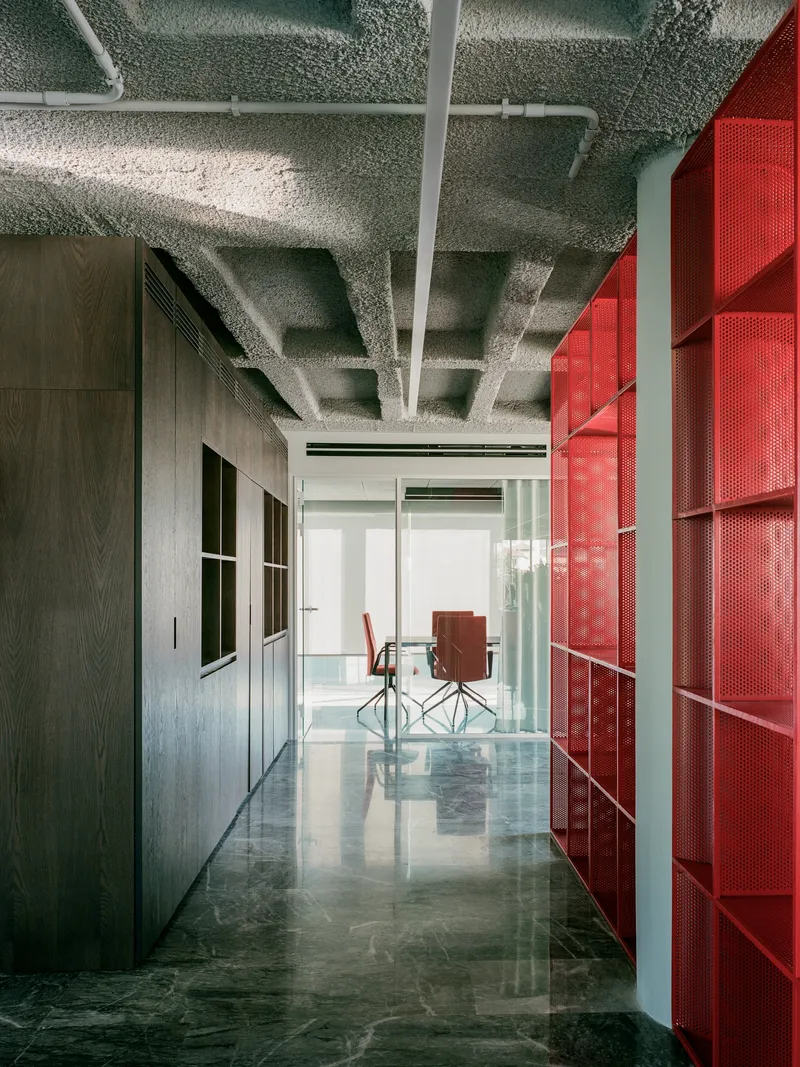 Corridor with exposed concrete ceiling, reflective green floor, and red perforated metal wall panels