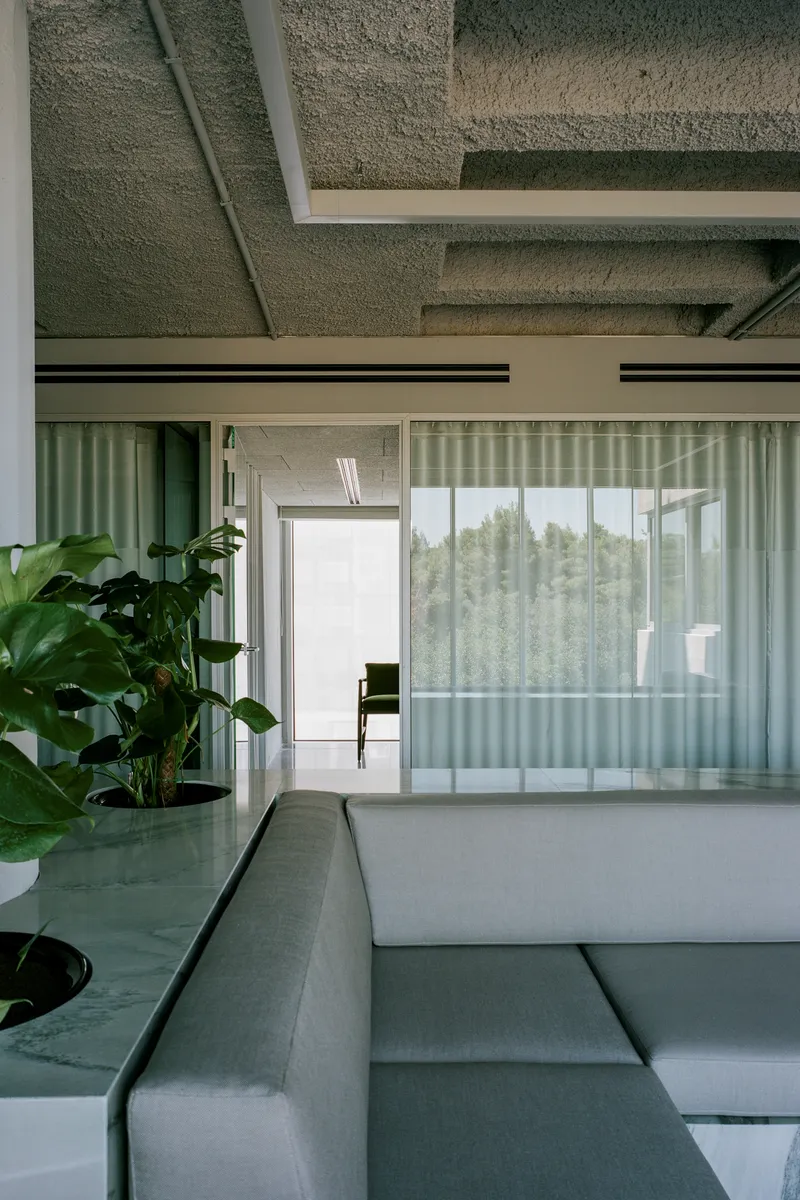 View through translucent pleated curtain partitions with potted plants framing the sunlit corridor beyond