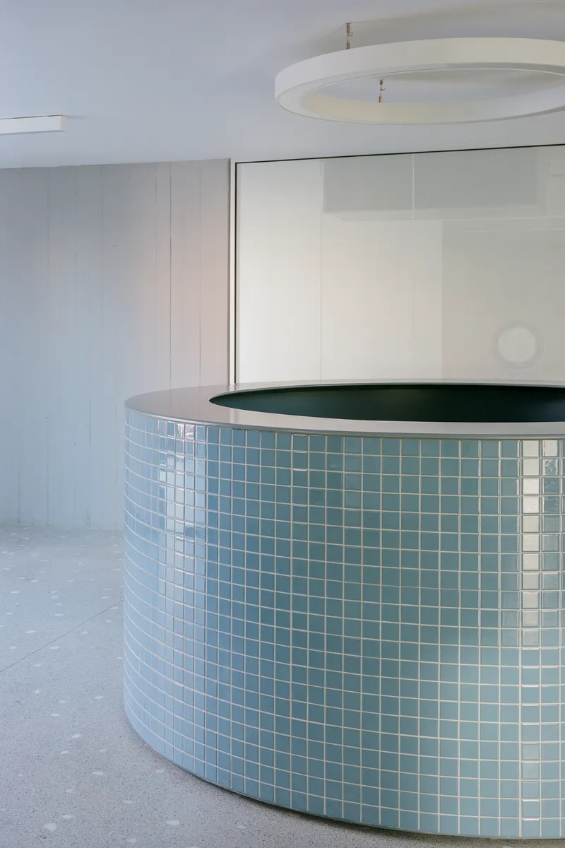Curved reception desk clad in pale blue mosaic tile beneath a circular pendant light