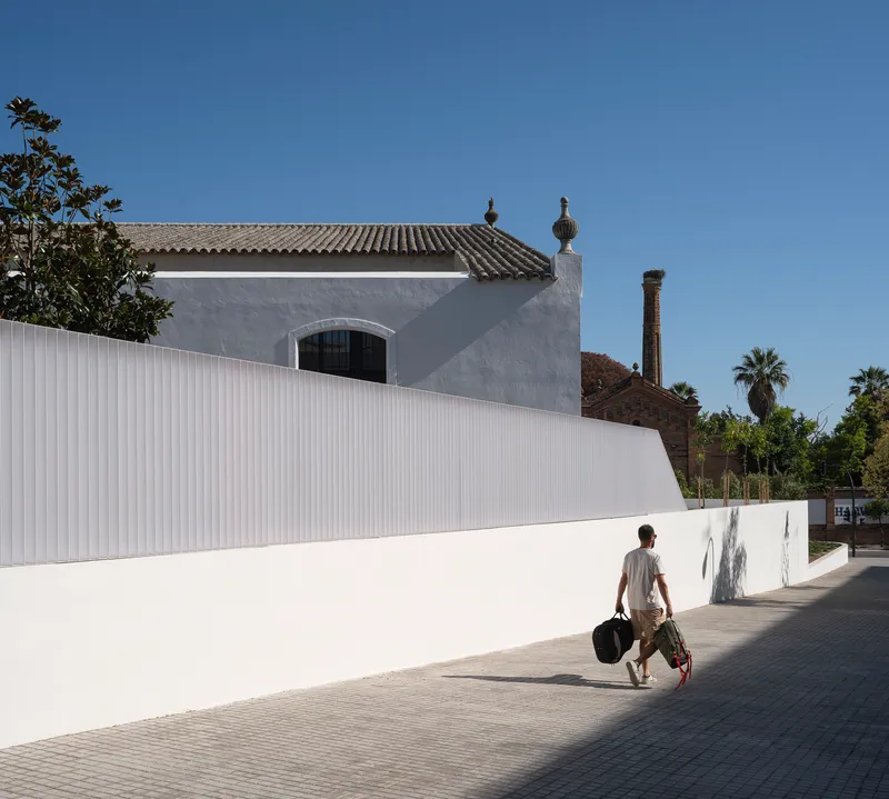 Pedestrian sidewalk and the white perimeter wall along the bodega's edge
