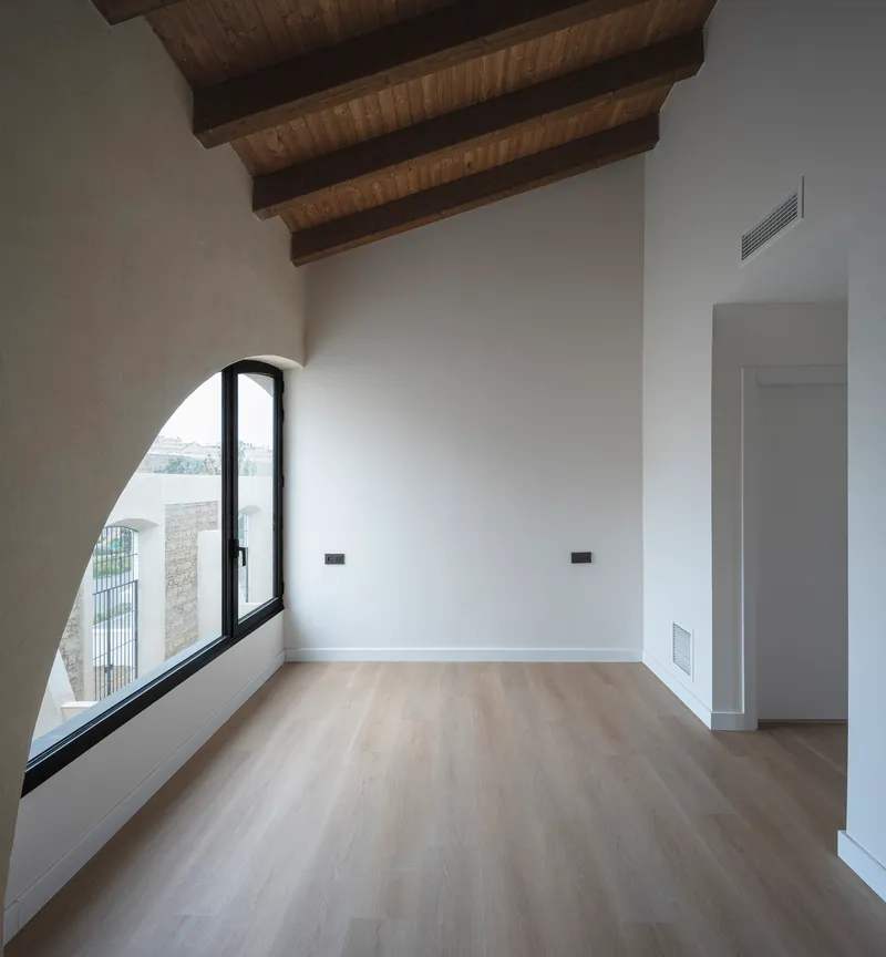 Empty bedroom with arched window, timber ceiling and oak floor