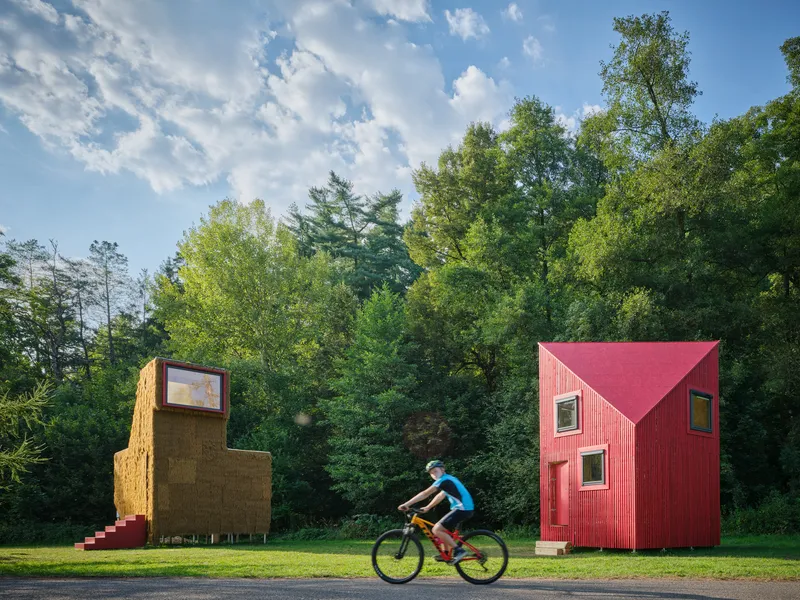 Two small pavilions on a grass lawn with a cyclist passing on the adjacent roadway