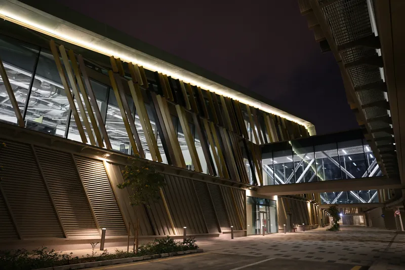 Entry canopy with angled metal fins and backlit soffit above the paved plaza at night