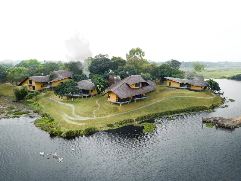 Aerial view of yellow-walled pavilions with thatched roofs clustered on a peninsula with rice terraces