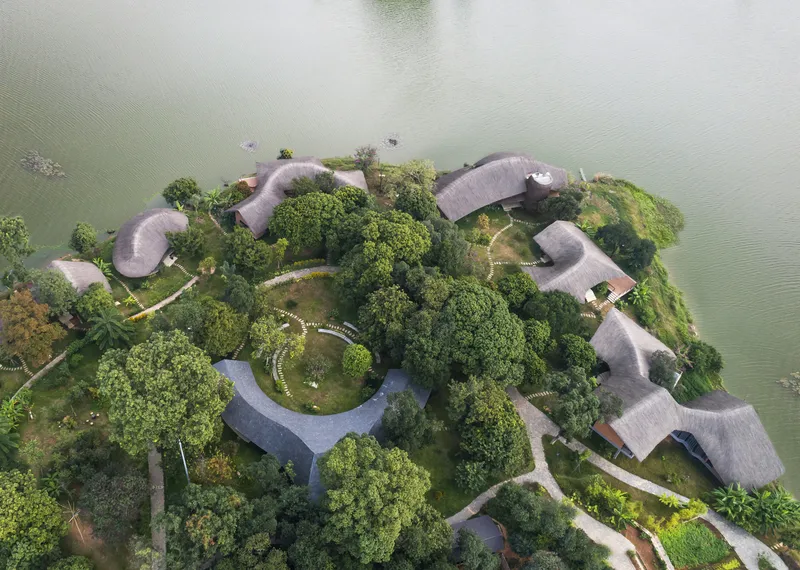 Overhead view of curving thatched roof structures arranged among dense trees on a river island