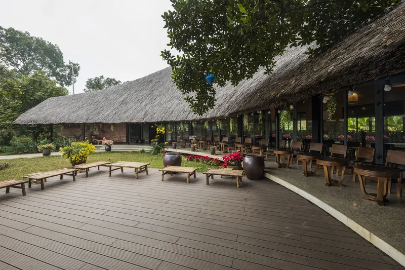 Timber deck terrace with low benches leading to a thatched-roof dining pavilion with open sides