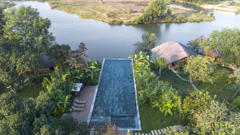 Rectangular swimming pool with dark tile overlooking the riverbank and surrounding agricultural fields at dusk