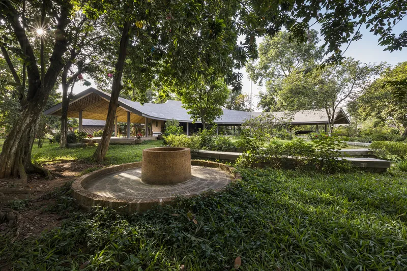 Circular earthen terrace with central well surrounded by planted beds under dappled tree shade