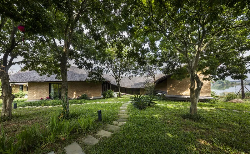 Low-slung brick volumes with thatched roofs arranged around a grassed courtyard with stepping stone path