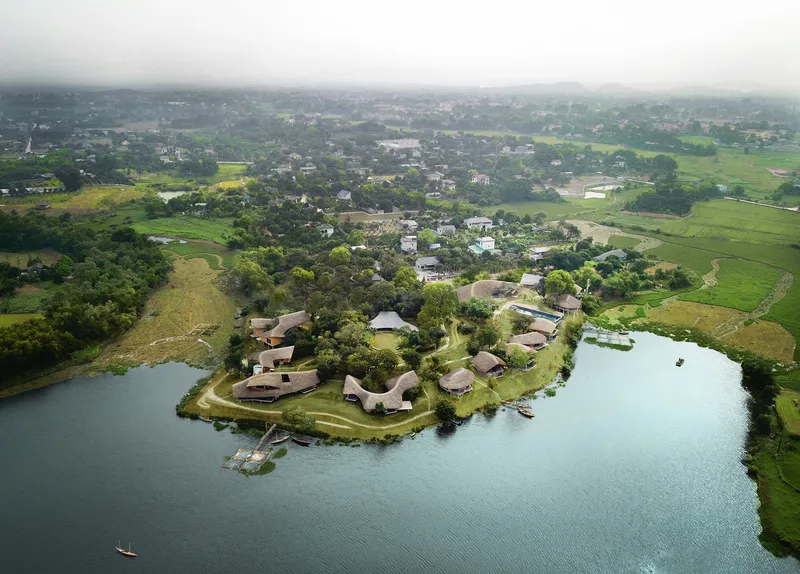 Aerial view of the thatched-roof pavilions clustered on a peninsula surrounded by a calm lake and green fields