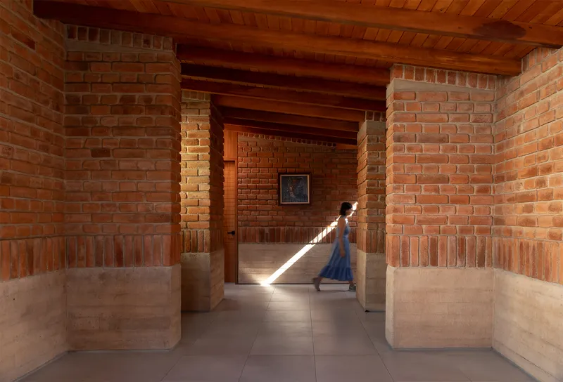 Interior corridor with exposed brick walls, timber ceiling beams and a figure walking through sunlight