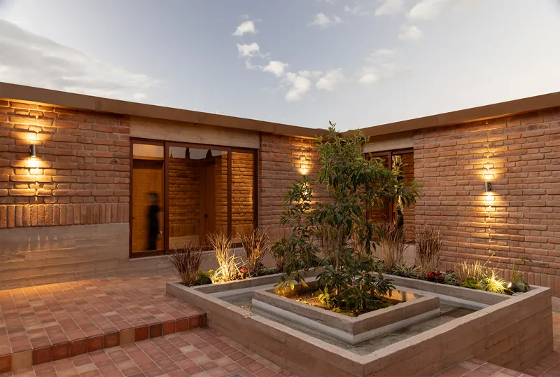 Interior courtyard with brick paving and central planted bed with a tree at twilight