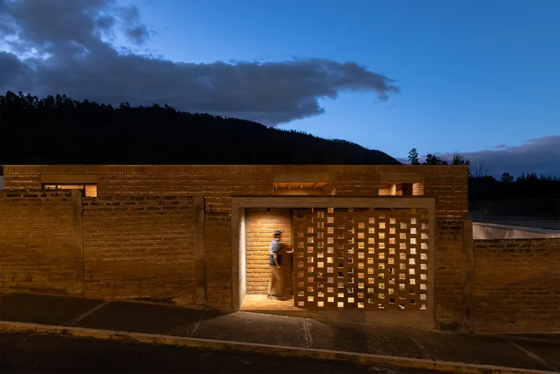 Brick facade with perforated screen entry wall illuminated at dusk with a person approaching
