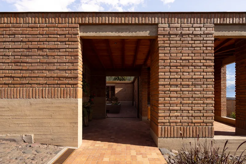 Covered entry passage through brick walls with terracotta tile floor and planted beds